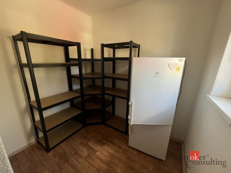 A room in a 4-room apartment with shelves, a refrigerator, and a wooden decor floor.