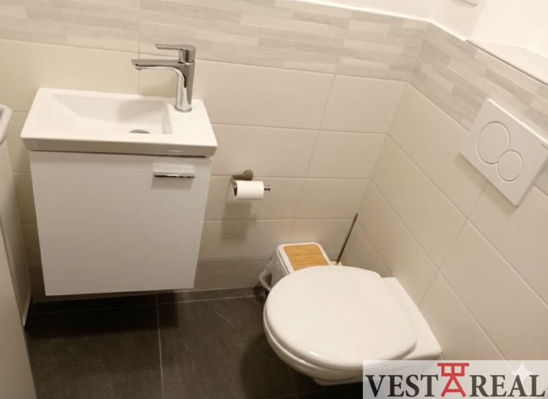 Bathroom in the office with a sink, toilet, and wall tiles.
