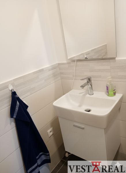 A sink with white tiles, a mirror, and a dark towel in an office.