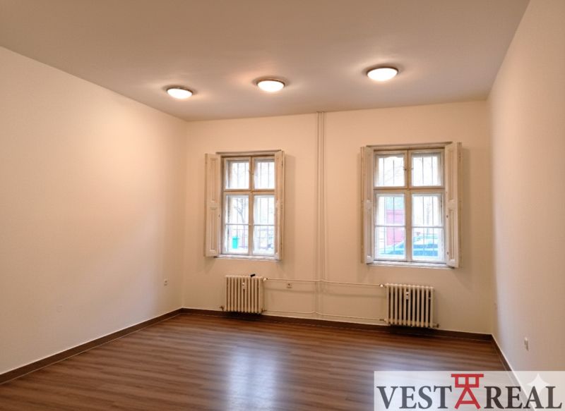 A room with two windows, white walls, and a wooden-patterned floor. Offices.