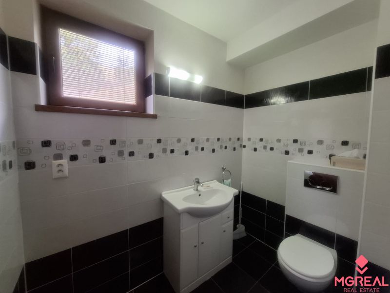 Bathroom with a sink and toilet in a family house, dark and light tiles.