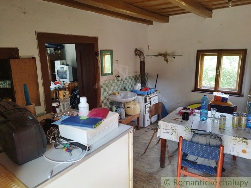 Interior of a cottage with a kitchen table, wood-patterned floor, and a tiled stove.