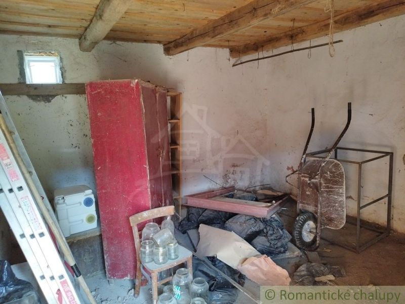 The interior of a cottage with a red wardrobe, a wheelbarrow, and wooden beams on the ceiling.