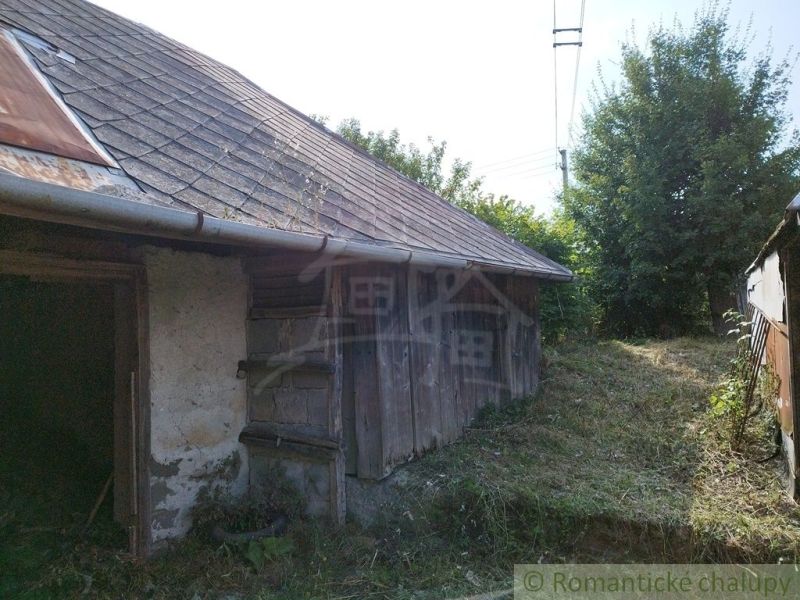 An old cottage in Hrušov with wooden walls and a shingle roof, surrounded by lush vegetation.