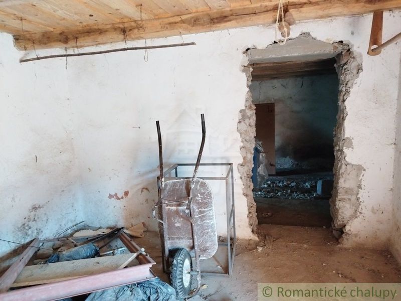 The interior of an old cottage with a cart, a wooden decor floor, and concrete walls.