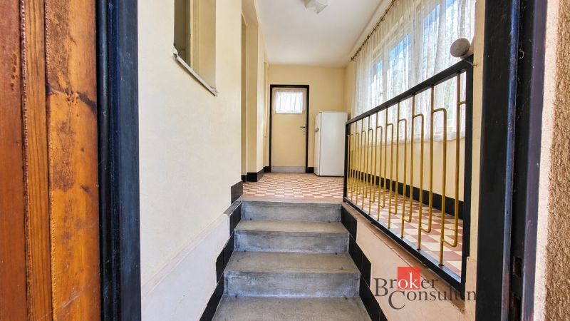 Hallway in a family house with stairs, railing, and tiles.