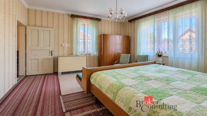 A bedroom in a family house with vintage furniture, wallpaper, and green curtains.