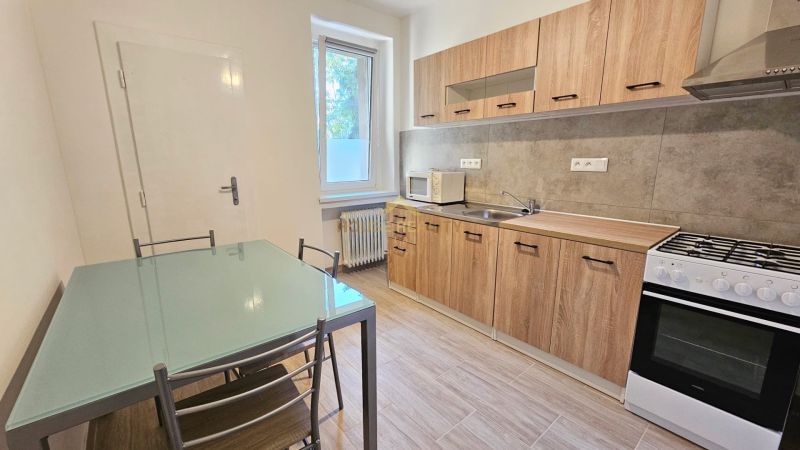 A kitchen in a 2-room apartment with a wood-patterned floor, a glass table, white walls.