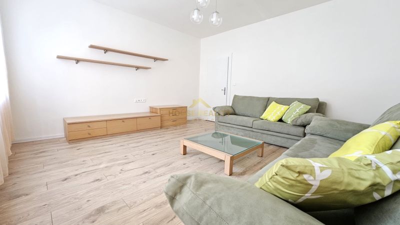 Living room of a two-room apartment with a couch, table, and shelves, floor with wooden decor.
