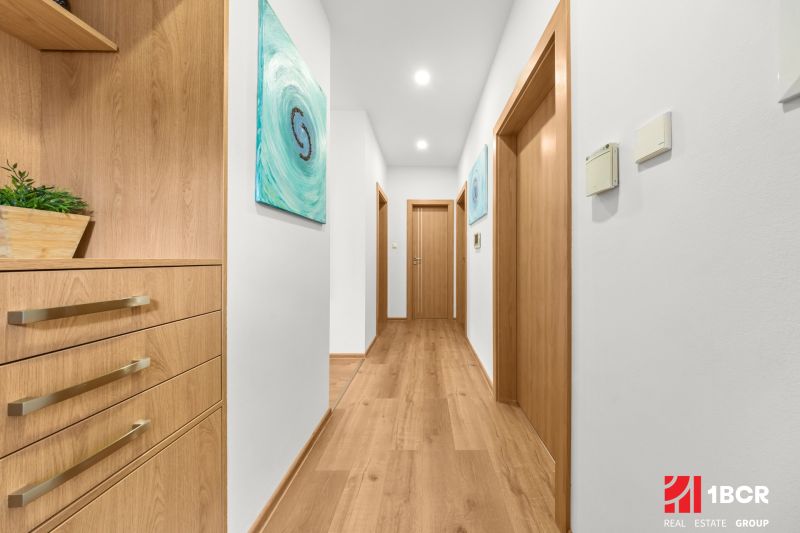 A bright hallway with a wood-patterned floor and wooden doors in a three-room apartment.