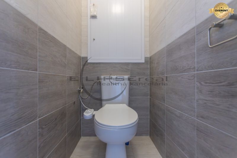 A toilet in a 3-room apartment with wood-patterned tiles.