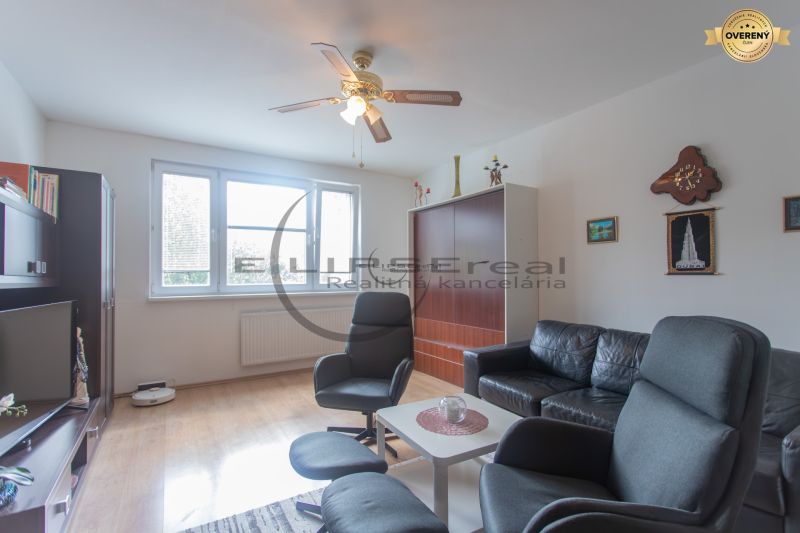 Living room in a 3-room apartment with a wooden decor floor, black sofa, and armchairs.