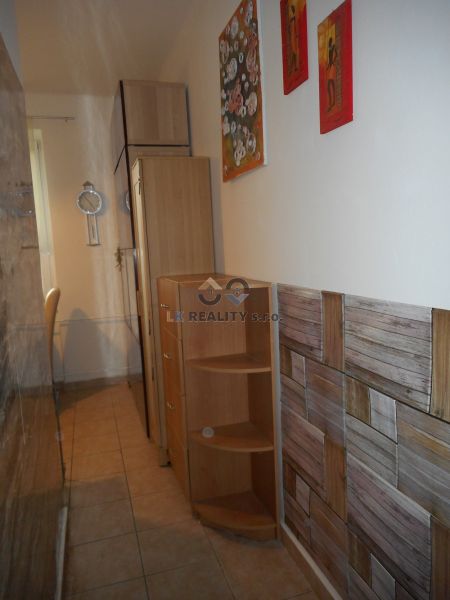 A narrow space in a 2-room apartment with wooden furniture and a tiled floor.