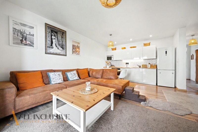 Living room with a sofa, kitchen, and wooden decor flooring in a family house.
