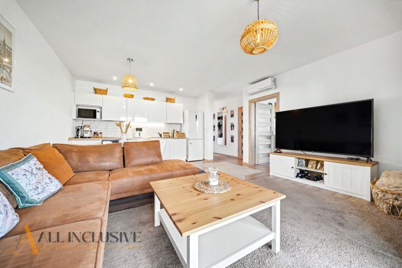 Living room in a family house with a leather sofa, television, and fully equipped kitchen.