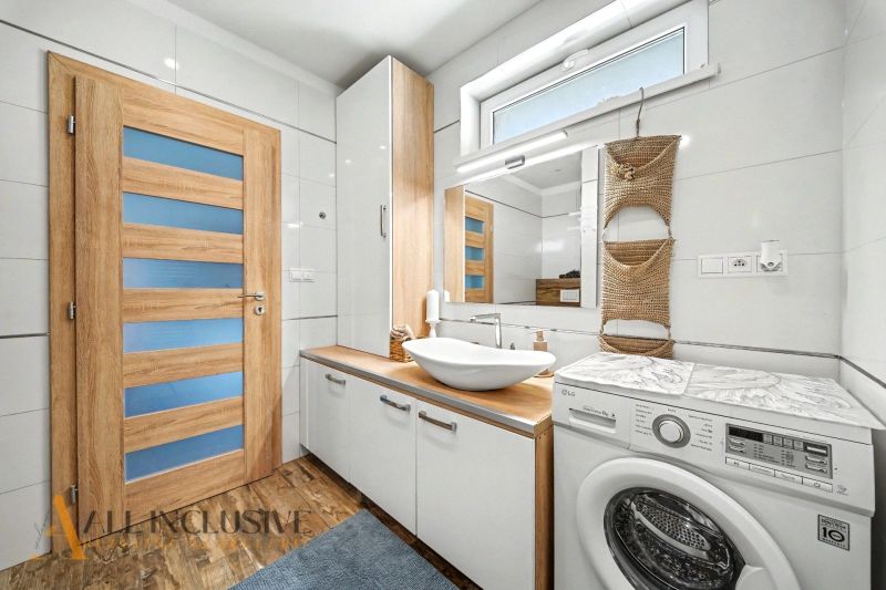 Bathroom in a family house with a washing machine, sink, and floor with wooden decor.