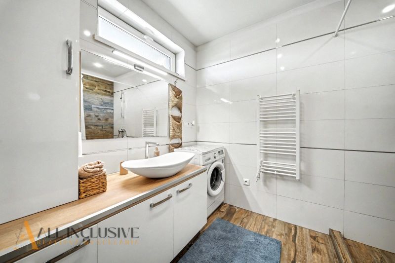 A bathroom in a family house with a sink, a washing machine, and a floor with a wooden decor.