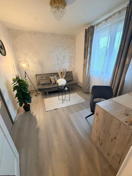A room in a 3-room apartment with a sofa, flowers, and a wooden decor floor.