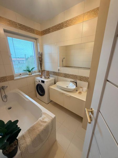 A bathroom with a bathtub, sink, and washing machine in a 3-room apartment with accessories.