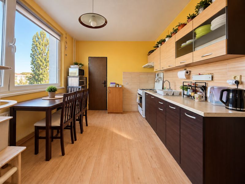 A kitchen in a 2-room apartment with a wooden decor floor and yellow walls.