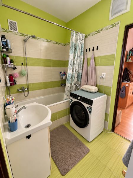 A bathroom with a bathtub, a washing machine, and green tiles in a 2-room apartment.