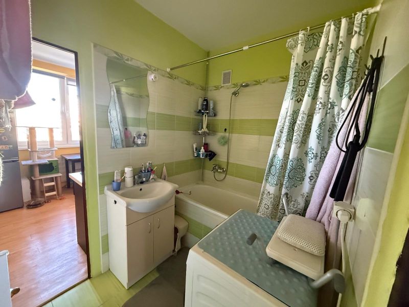 Bathroom in a two-room apartment with a bathtub, washing machine, and bathroom furniture.