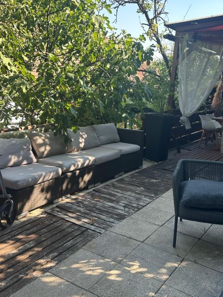 A terrace with comfortable seating, wooden flooring, and greenery in a 3-room apartment.
