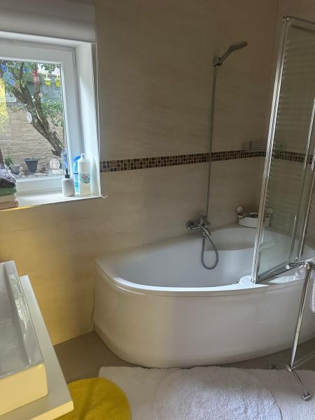 Bathroom with a bathtub, shower screen, and window in a 3-room apartment.