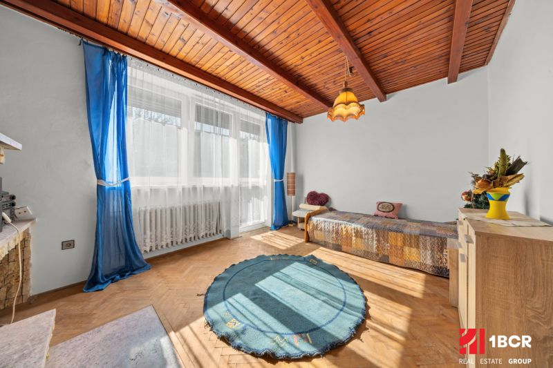 A room in a family house with a wooden decor floor, blue curtains, and a large window.