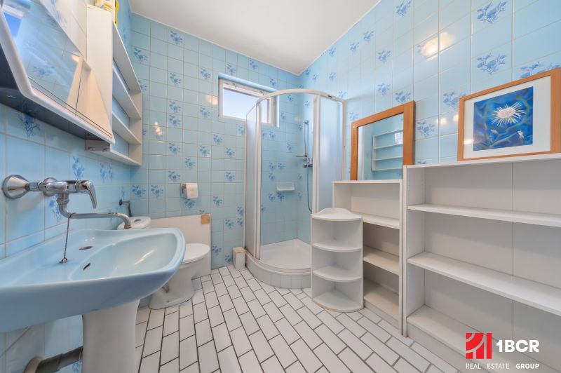 A bathroom with blue tiles, a shower enclosure, and white furniture in a family house.