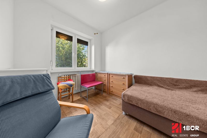 A room with a large window, a chair, a dresser, and a floor with a wooden decor in a family house.