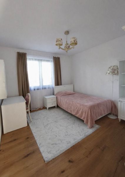 A bedroom in a family house with a bed, a desk, and a wooden decor floor.