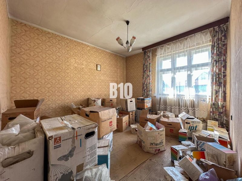 A room in a family house with cardboard boxes, wallpaper walls, wood-decorated floor, curtains.