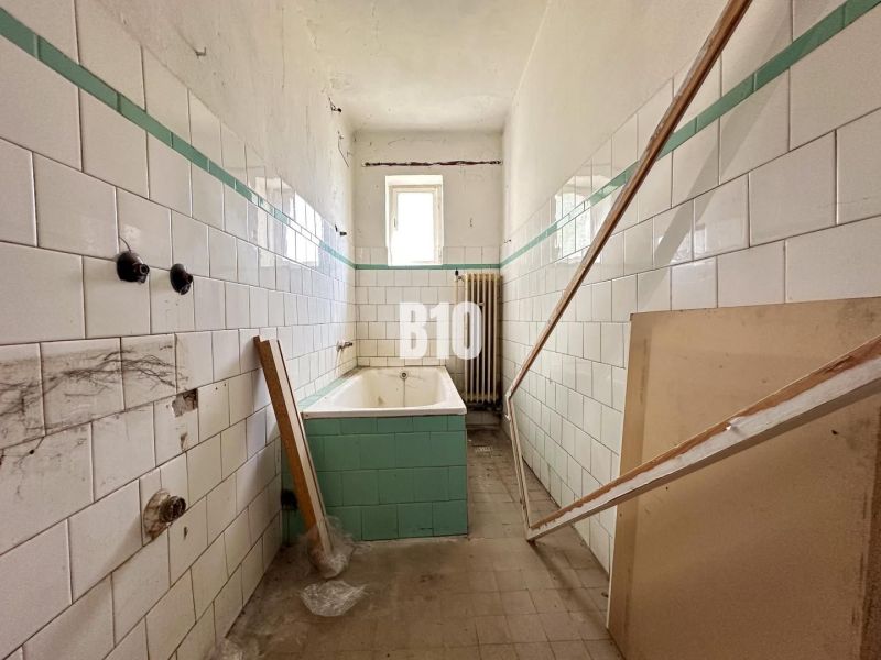 A family house bathroom with worn-out tiles and a bathtub awaiting renovation.