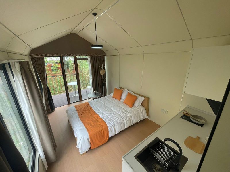 A cottage with a wooden floor decor, a simple bed, a small kitchenette, and a balcony.