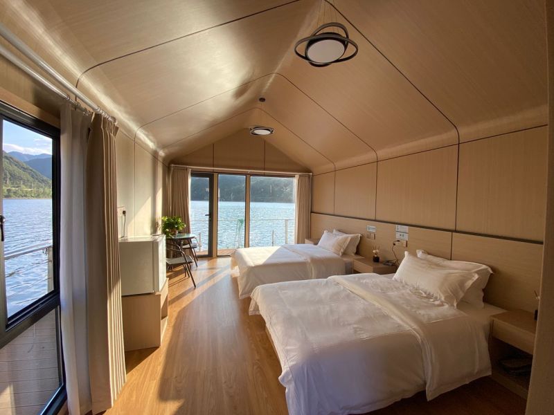 A bedroom in a cabin with two beds and a wooden decor floor, overlooking a lake.
