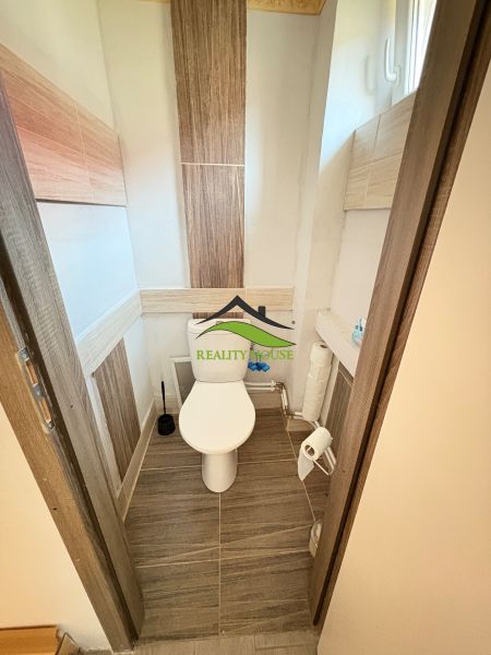 A toilet in a family house with ceramic tiles and a narrow window.