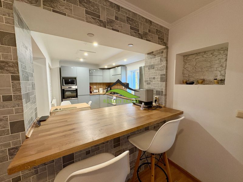 A kitchen in a family house with a bar counter and gray cabinets, flooring with a wooden decor.