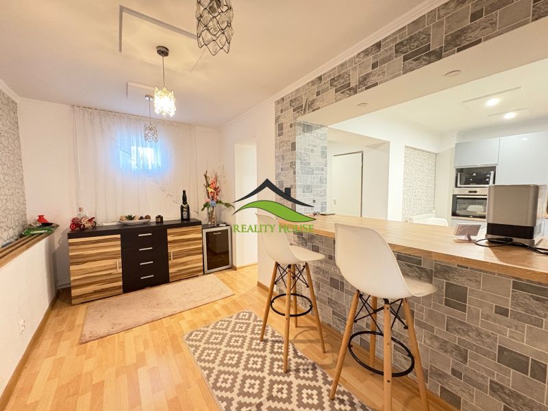 Interior of a family house with a bar counter, white chairs, and a floor with a wooden decor.