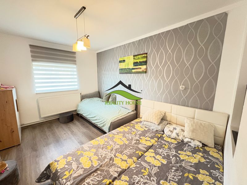 A bedroom in a family house with a wooden decor floor and patterned wallpaper on the wall.