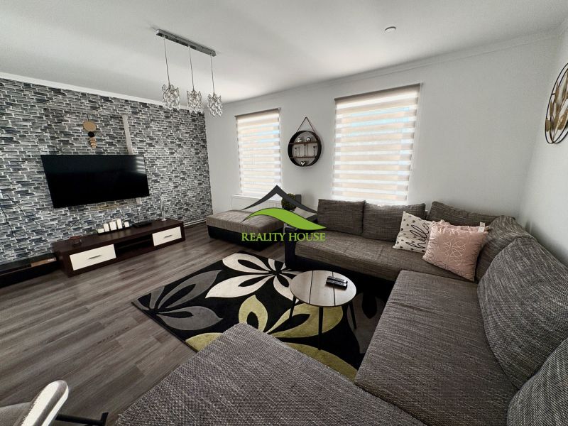 Living room in a family house with wood-patterned flooring, a large sofa, and a patterned rug.