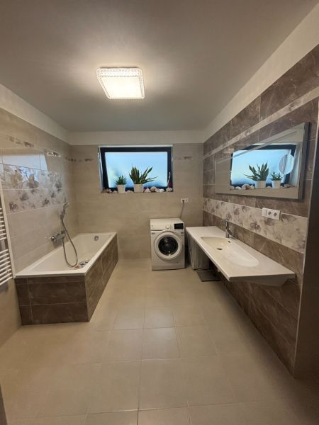 A bathroom in a family house with a shower, bathtub, washing machine, and mirror on the tiles.