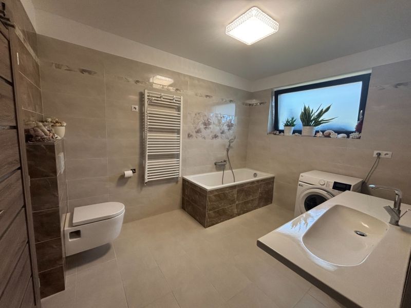 A bathroom in a family house with a bathtub, sink, and washing machine, in soft beige tones.