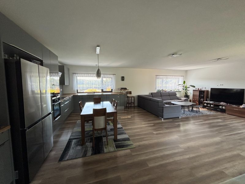 Open interior of a family house with a kitchen, dining table, sofa, and wooden decor flooring.