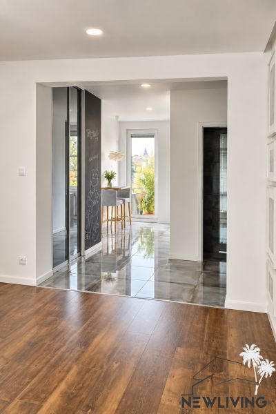 The 3-room apartment has a floor with a wooden decor and a bright kitchen in the background.