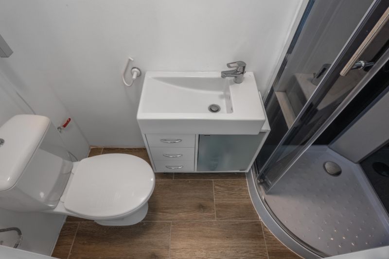 The bathroom includes a shower, a sink, and a toilet, with a floor in a wooden design.