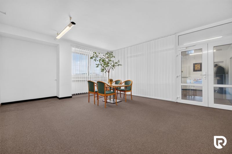 Offices with carpet, a desk and chairs, glass doors and a large window.