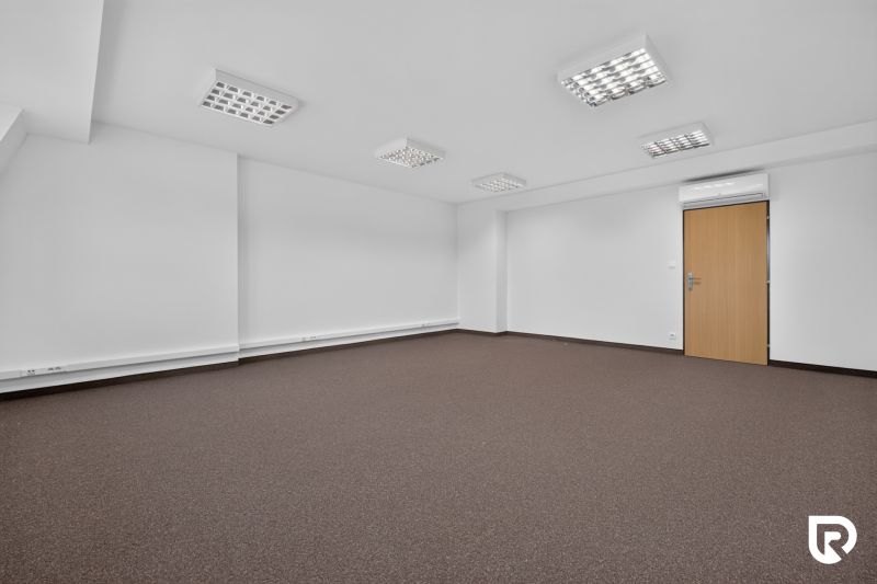 Empty office with brown carpet and white walls, the room is lit and has air conditioning.