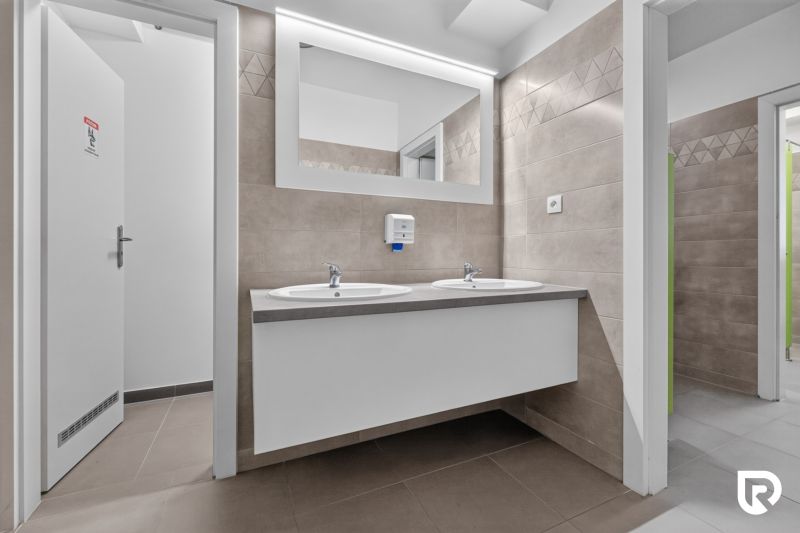 Offices with ceramic tiles, double sink, and large mirror.