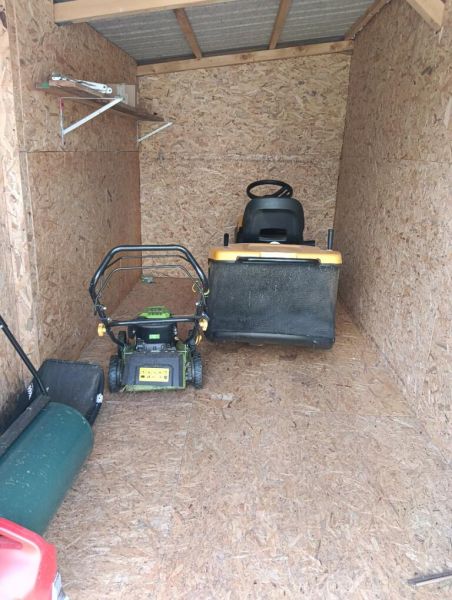 A wooden shelter with garden equipment including lawnmowers in the gardens.
